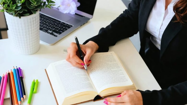 Professional writing thoughtfully in a journal surrounded by colorful pens and a laptop, embodying the practice of journaling for enhancing emotional intelligence.