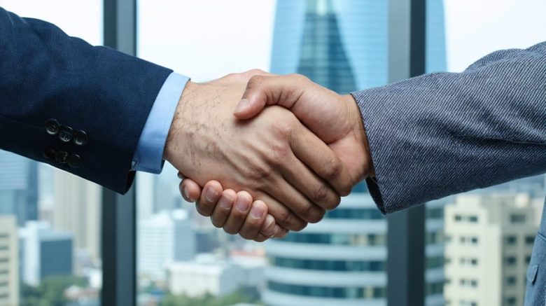 "Two professionals of diverse backgrounds shaking hands in a bright modern office setting."